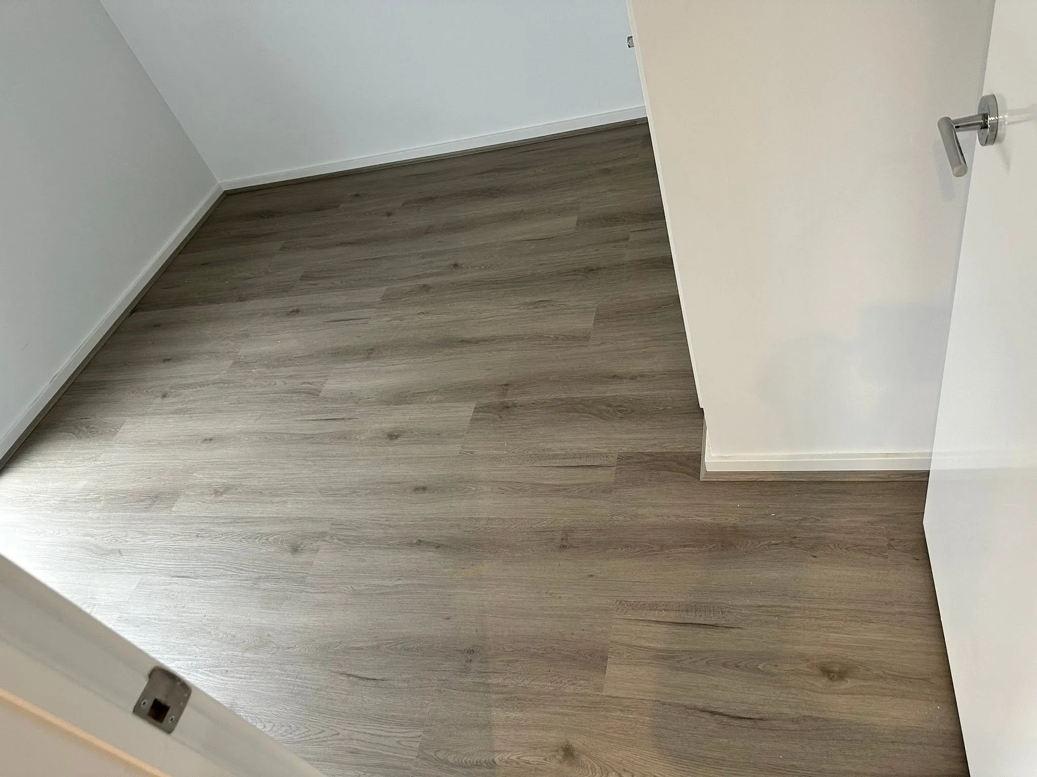 Tan Oak hybrid flooring in a room with white walls and a door
