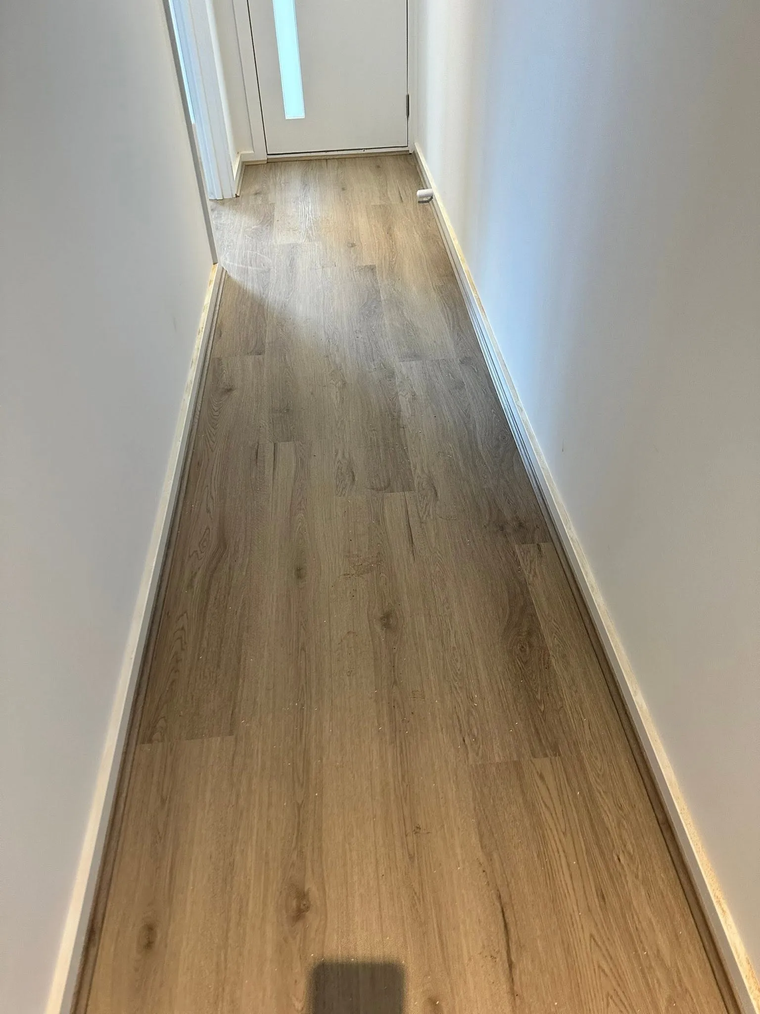 Tan Oak hybrid flooring running down a hallway to a door with a glass panel