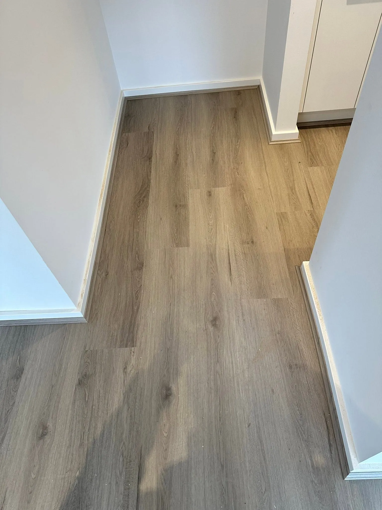 Tan Oak hybrid flooring laid neatly around wall corners and skirting near the kitchen