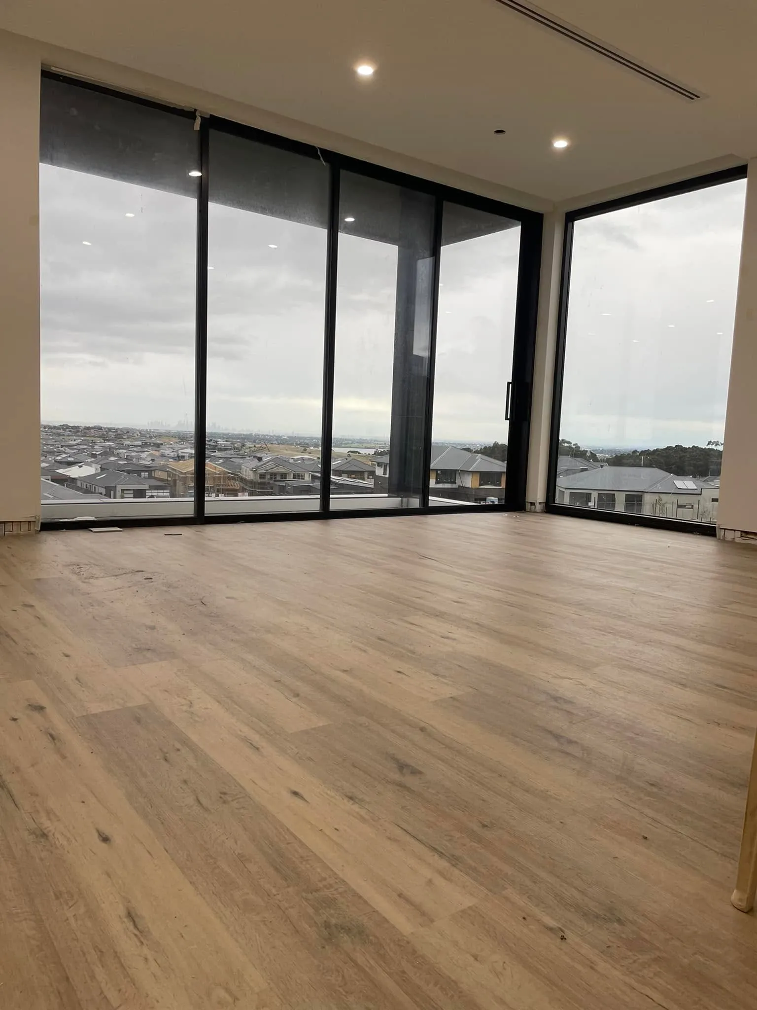 Light timber-look flooring in an apartment with floor-to-ceiling corner windows over suburban Melbourne
