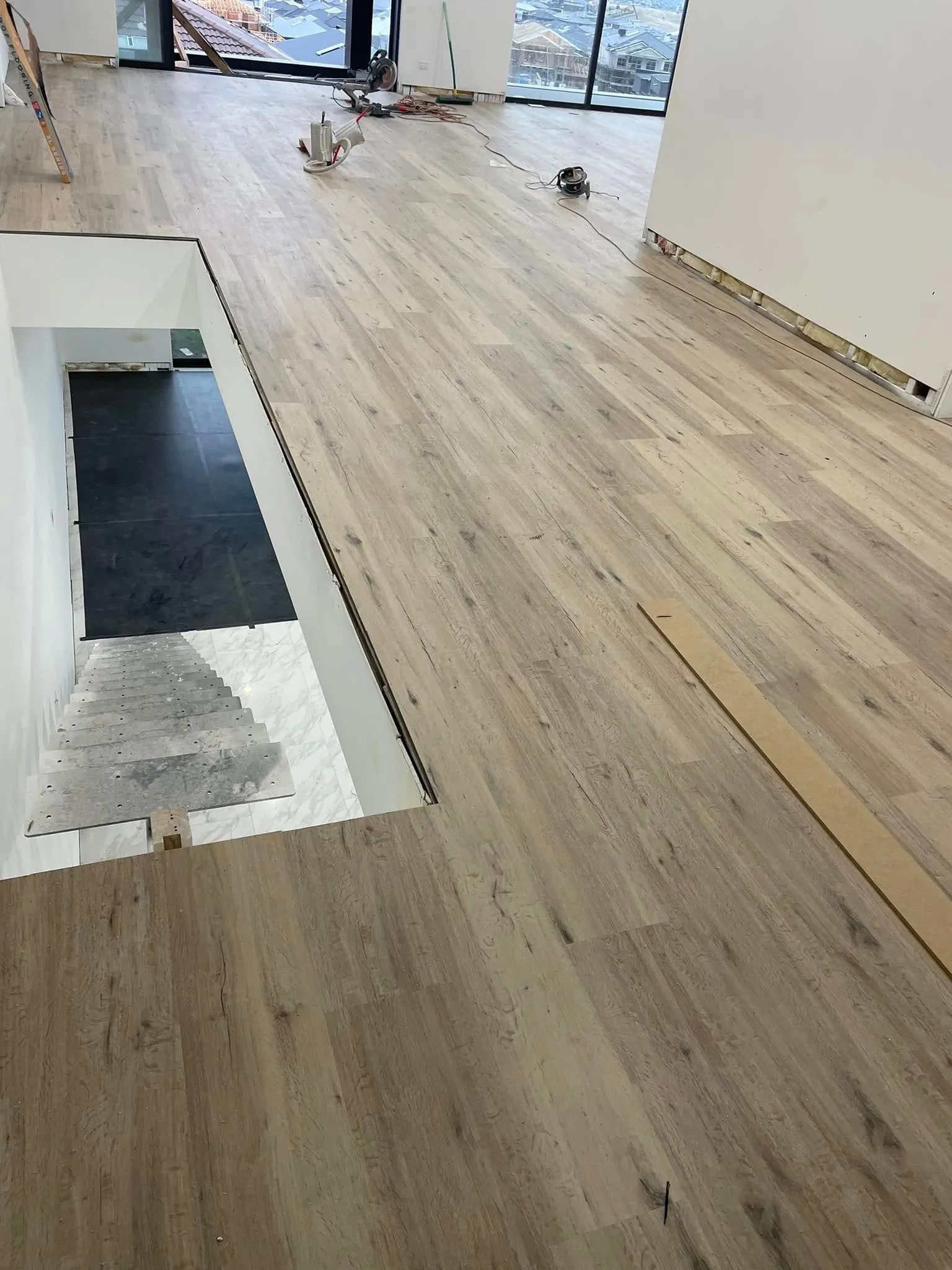 Light timber-look flooring partway through installation in an apartment, with tools on the floor