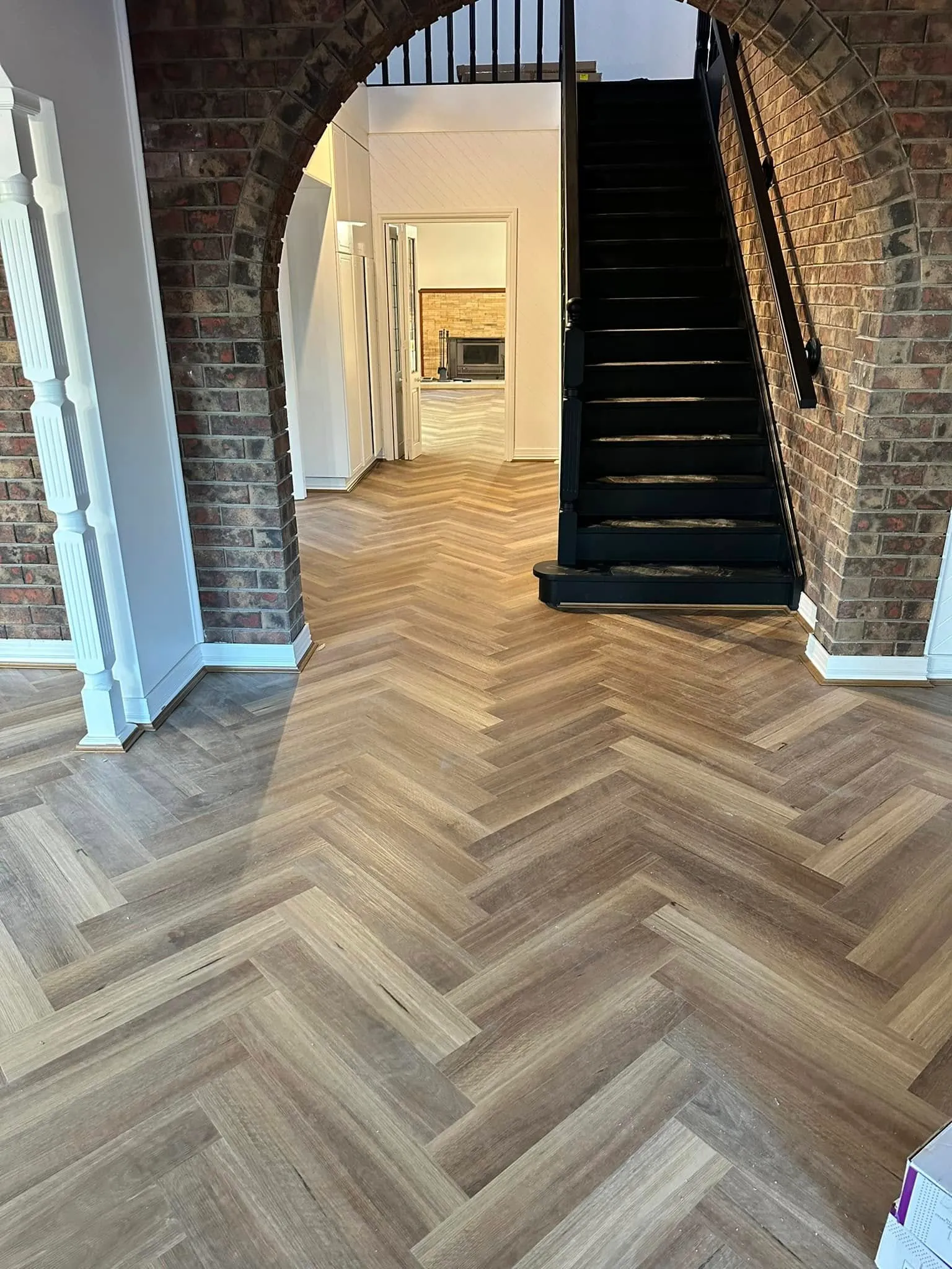 Grey-brown herringbone flooring under a brick archway beside a staircase