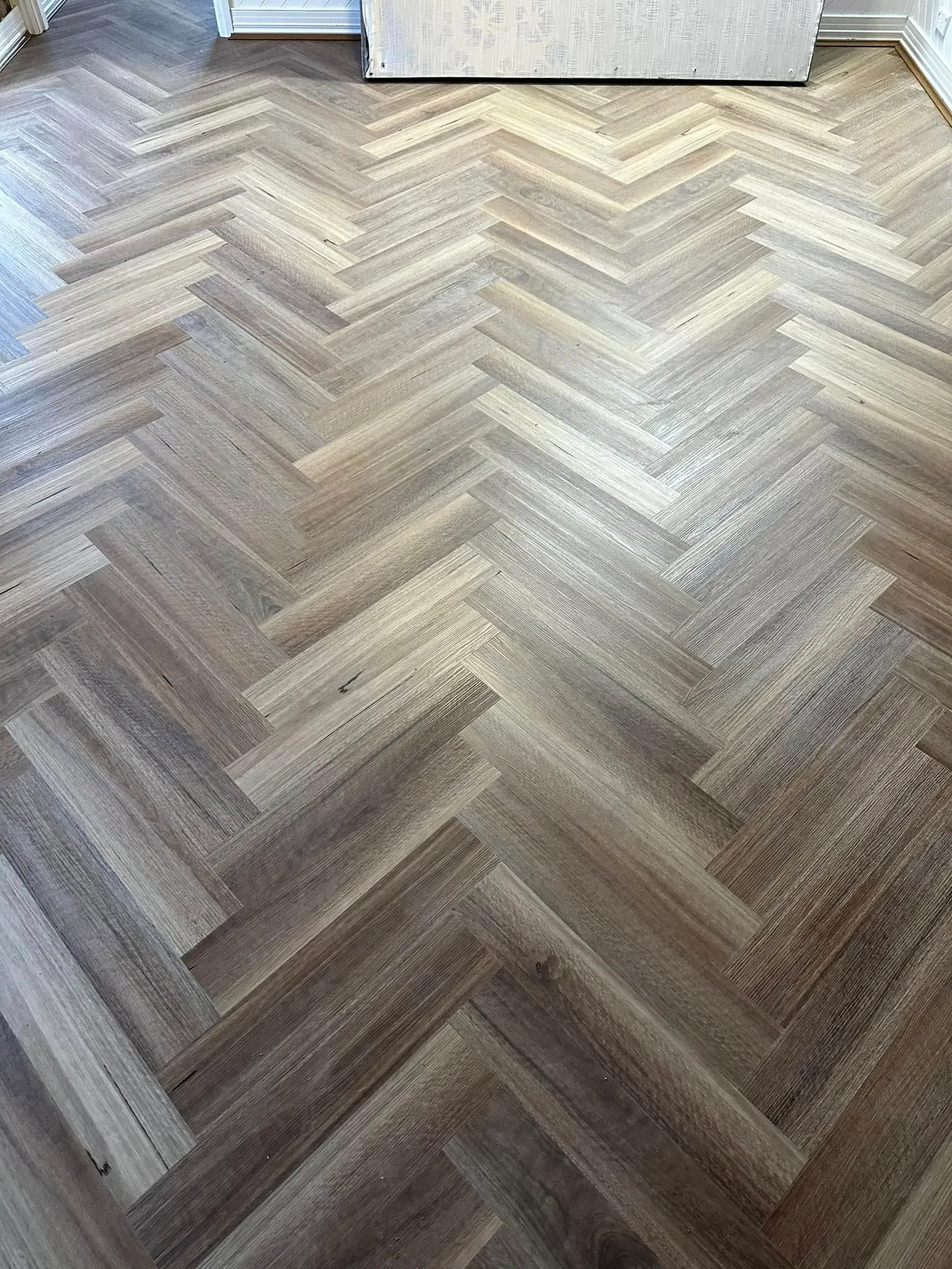 Grey-brown herringbone flooring near a doorway with wallpapered walls
