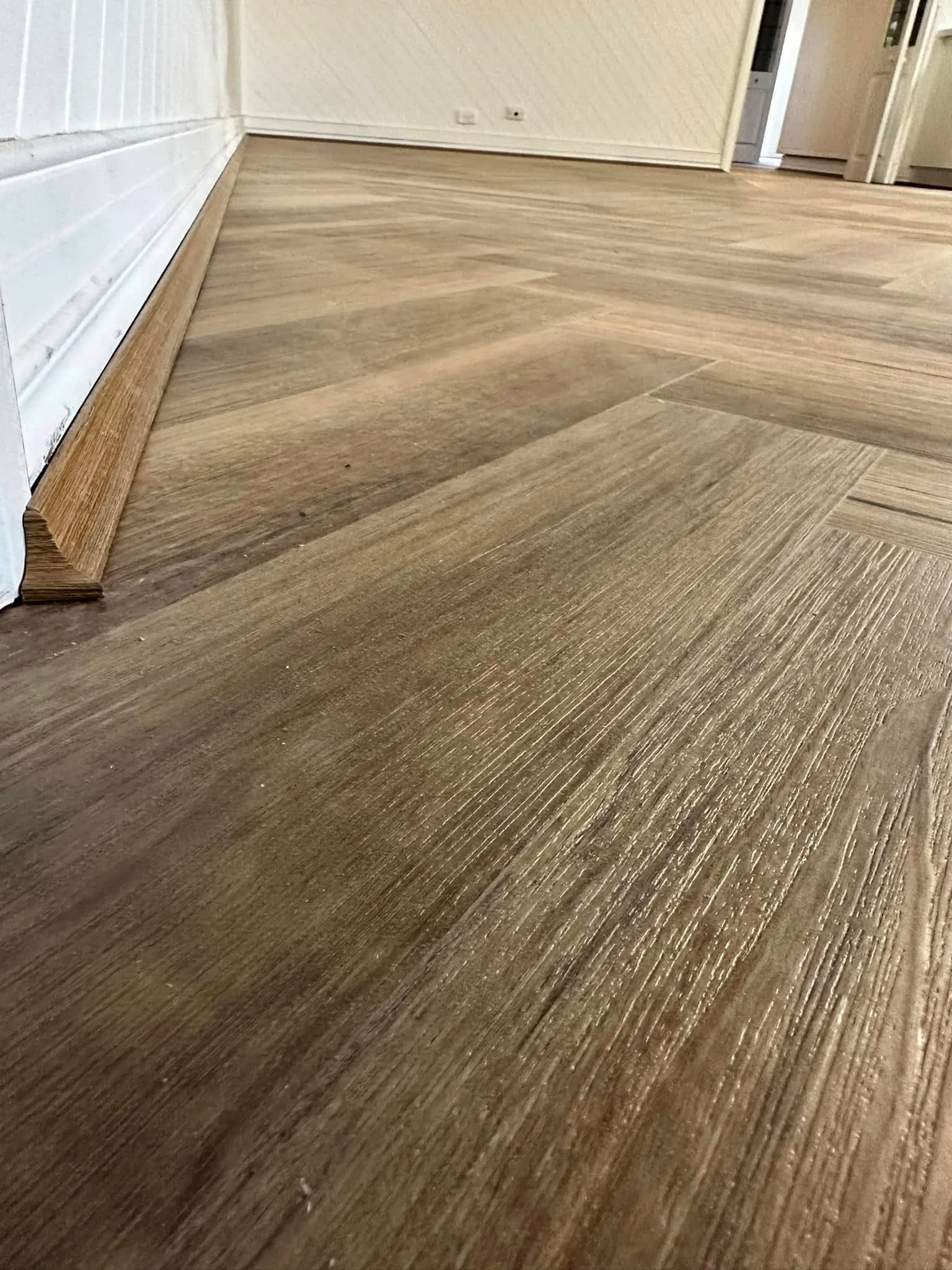 Grey-brown herringbone flooring running down a hallway