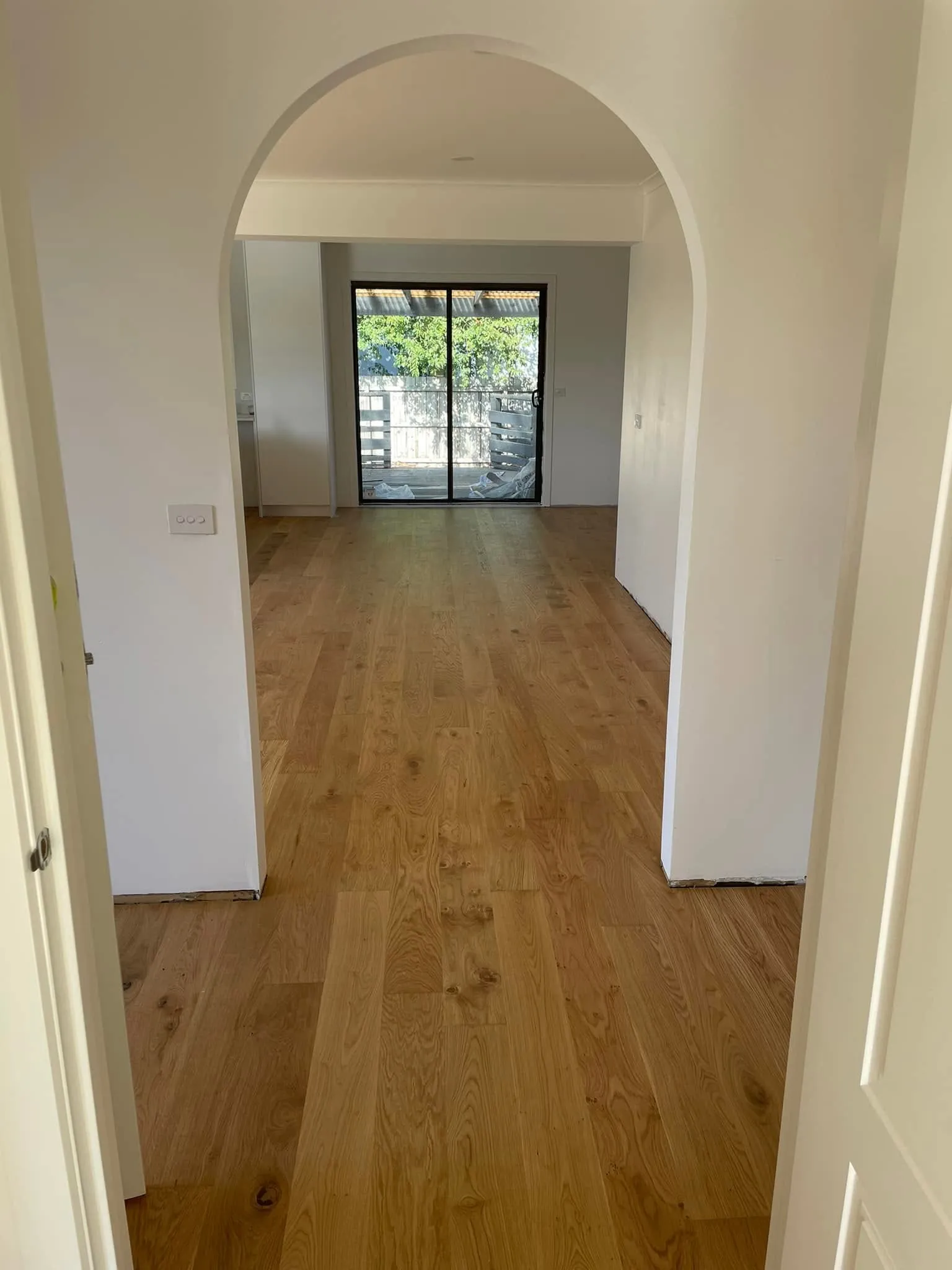 Honey-toned oak flooring seen through an arched doorway to a living room